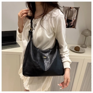 Detail of black faux leather tote with golden metal logo on the front strap and bag
