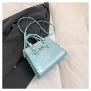 Detail view of light blue structured handbag with golden hardware on a grey blazer