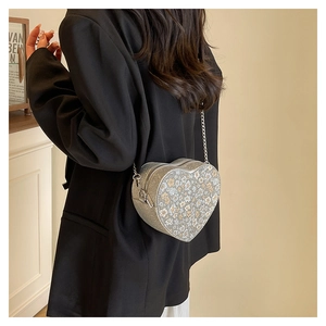 Detail shot of heart-shaped silver sequin bag with floral accents and chain strap on model