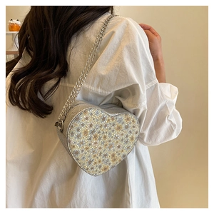 Detail of silver heart-shaped sequin crossbody bag with chain strap worn by a model