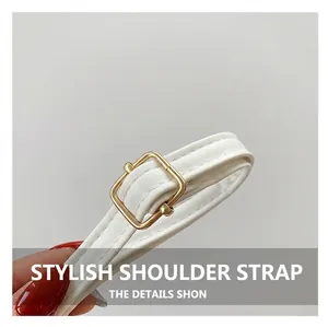Detail view of a white leather strap with a polished golden metal buckle and stitching