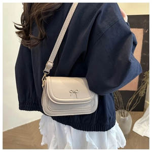 Detail of beige crossbody bag with metal bow accent shown on model back view