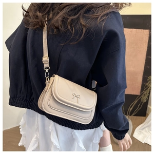 Detail of cream white leather crossbody bag with a small golden metal bow clasp