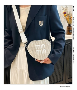 Detail of white heart-shaped straw bag with embroidered letters and wide shoulder strap