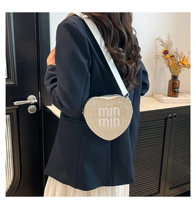Detail of heart-shaped straw crossbody bag with white logo strap worn by a model