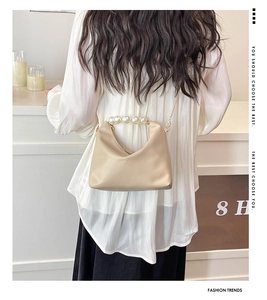 Detail of elegant beige crescent bag featuring large pearls handle and gold chain strap