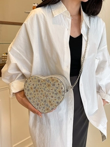 Sparkly heart shaped chain bag with floral sequin patterns worn by a model