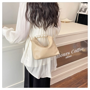 Detail view of large decorative pearls on the handle of a cream-colored leather handbag