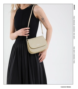 Detail of champagne gold saddle bag with textured finish and silver logo on black dress