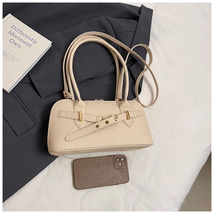 Top view of beige baguette bag with woven texture, metal buckle detail on white bedding