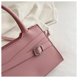 Détail du sac à main en cuir rose mat avec sangles décoratives et boucle carrée argentée