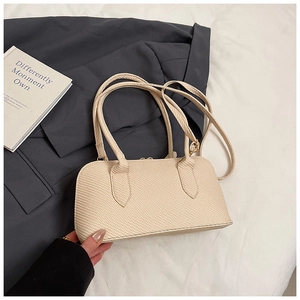 Detail of beige textured shoulder bag with dual handles and strap on grey blazer