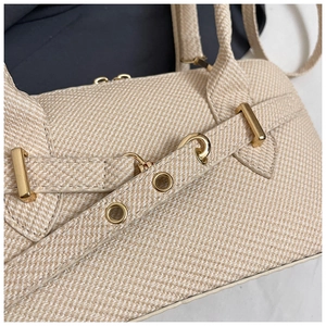 Close-up of beige woven texture handbag featuring polished gold metal ring hardware
