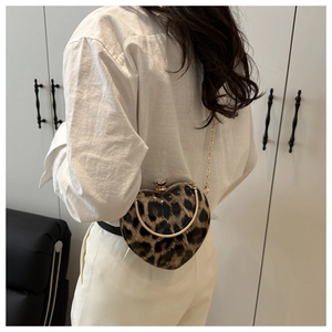 Detail of heart-shaped leopard print clutch with gold chain strap worn by a model