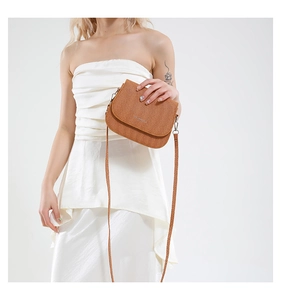 Detail of brown woven texture saddle bag with a minimalist metal logo on the front flap