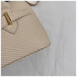 Detail of beige woven fabric texture and gold rectangular buckle on minimalist bag