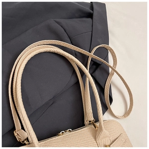 Detailed macro view of beige woven texture on a shoulder bag with gold hardware accents