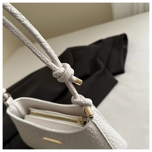Dettaglio borsa a tracolla bianca intrecciata con zip dorata e accenti di tracolla annodata