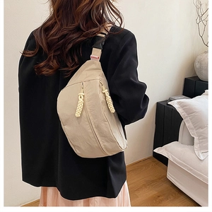 Detail of beige crossbody bag featuring dual zippers and wide shoulder strap with buckle