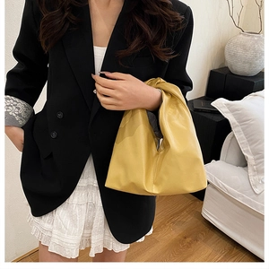 Sac à main plissé jaune vif porté avec un blazer noir et une jupe blanche au style urbain