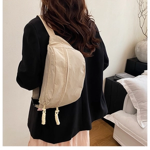 Detail of beige nylon crossbody bag with dual zippers and woven cord pullers