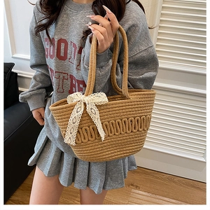 Detailed view of woven straw tote bag featuring white lace trim and bow accent