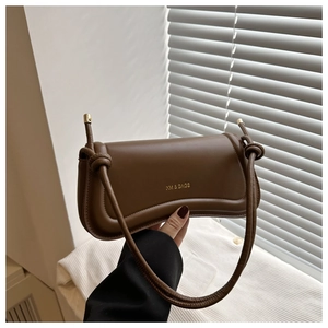 Detailed view of brown leather shoulder bag with gold logo and decorative knot strap