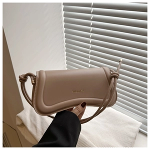 Detail of a khaki underarm bag featuring a unique knotted strap and gold logo finish
