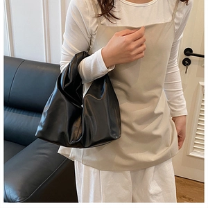 Gros plan d'un sac hobo plissé en similicuir noir porté par un mannequin dans une pièce