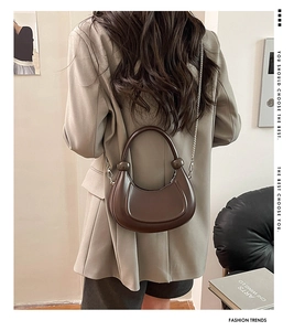 Detail of dark brown crescent bag with decorative ball handle and metal chain strap