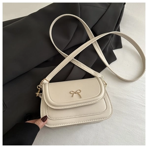 Detailed view of the gold bow metal buckle on a cream beige crossbody flap handbag