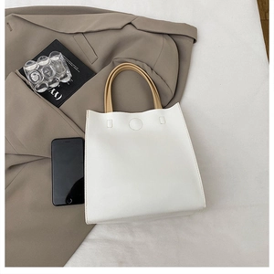 Detail of minimalist white leather tote bag with contrasting tan handles and stitching