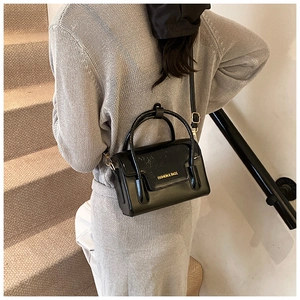Close-up of a black patent leather square bag featuring golden lettering on a stair scene