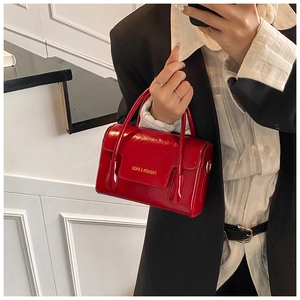 Detail of red oil wax leather handbag showing glossy texture and golden fashion lettering