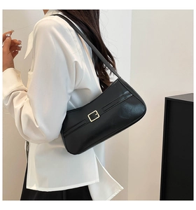 Detail view of a black leather shoulder bag featuring a gold buckle on model