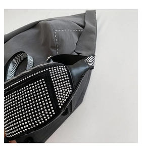 Detail of black chest bag with silver round rivets and V-pattern woven strap