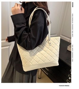 Close-up of white quilted tote bag featuring silver bow charm and rivet detail