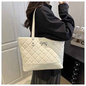 Detail of a beige quilted tote bag with silver bow accent and slim double shoulder straps