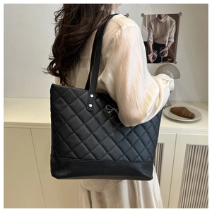 Detail of black quilted tote bag with silver bow accent and rivet handle attachment