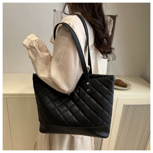 Detail of black quilted tote bag with silver bow pendant and long double shoulder straps
