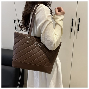Side view of a brown quilted tote bag with silver bow detail shown on a model
