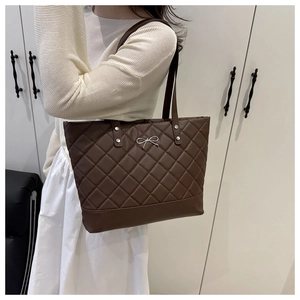 Detail of deep brown quilted tote bag with silver bow hardware and thin straps