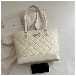 Detail of beige quilted tote bag with silver bow accent and elegant diamond stitching