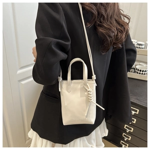 Détail du mini sac carré blanc avec nœud décoratif et poignée sur une veste noire