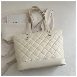 Detailed close-up of quilted pattern and silver metal rivets on the cream tote bag