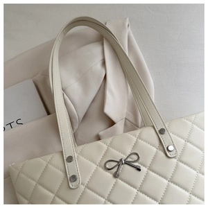 Detail of cream quilted tote bag featuring a silver metal bow and rivet accents