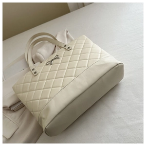 Detail of beige quilted tote bag featuring a silver bow pendant and elegant top handles