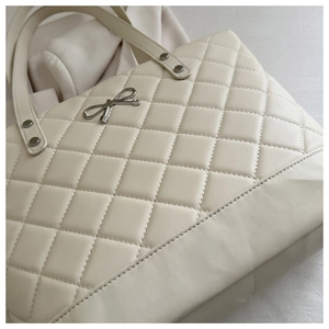 Close-up of quilted cream tote bag featuring a silver metal bow and refined PU leather