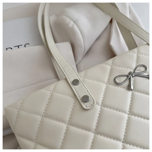 Detail of quilted beige tote bag showing silver bow ornament and fine stitching quality