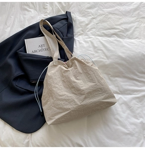 Sac fourre-tout beige à cordon bleu posé sur un drap blanc à côté d'un livre d'art